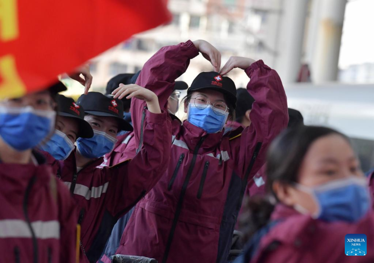 Medical workers in masks and red jackets making heart shapes with their arms