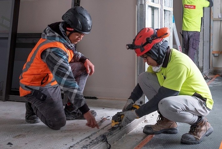 Two construction workers in safety gear working on a concrete floor