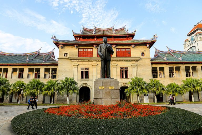 Historic Xiamen University building with a statue and flower garden in front