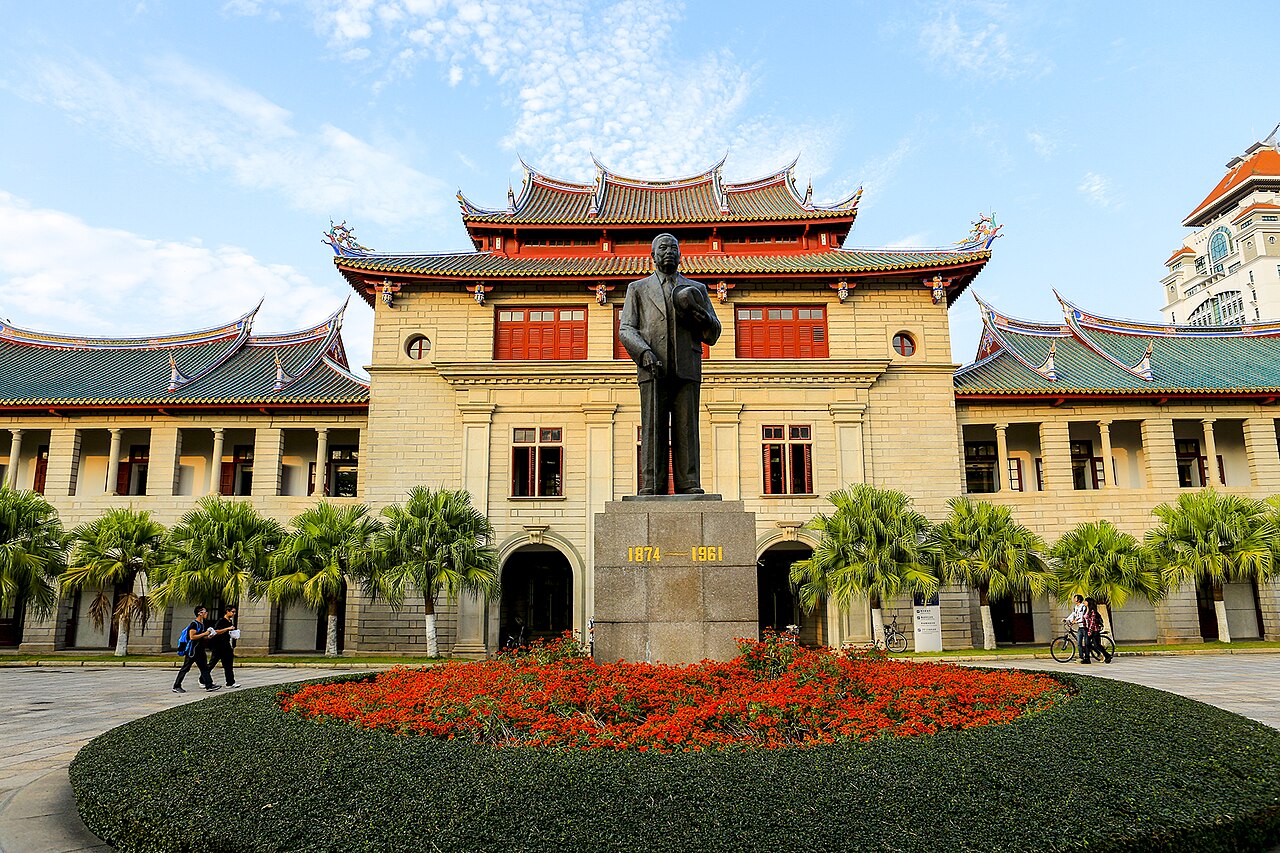 Historic Xiamen University building with a statue and flower garden in front