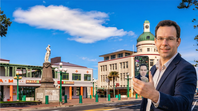 A man taking a selfie on a phone in front of Art Deco buildings in Napier